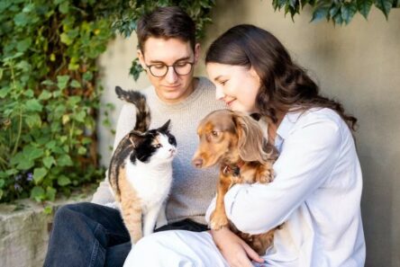 Young couple sitting outdoors with a calico cat and a dachshund, natural pet wellness UK