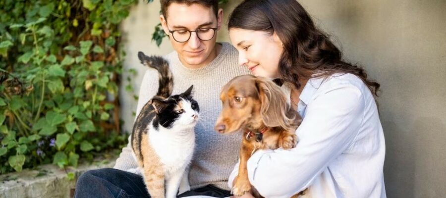 Young couple sitting outdoors with a calico cat and a dachshund, natural pet wellness UK